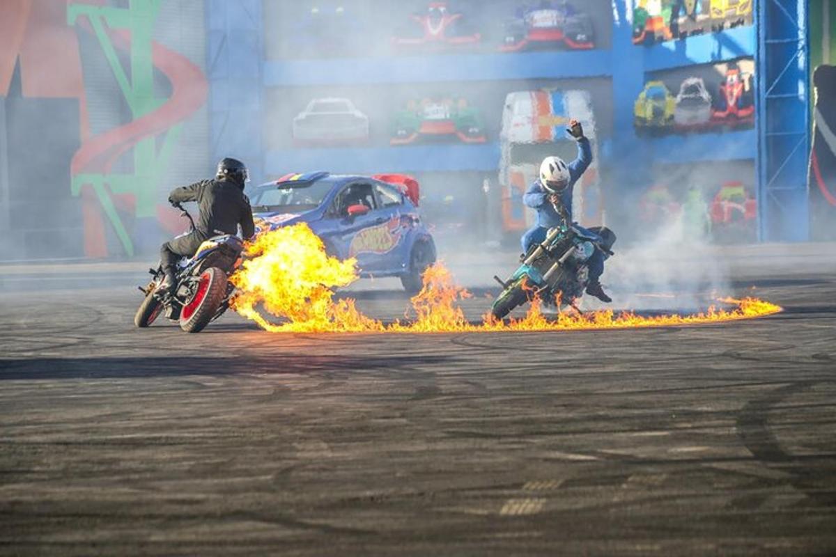 two people riding motorcycles on a track with fire