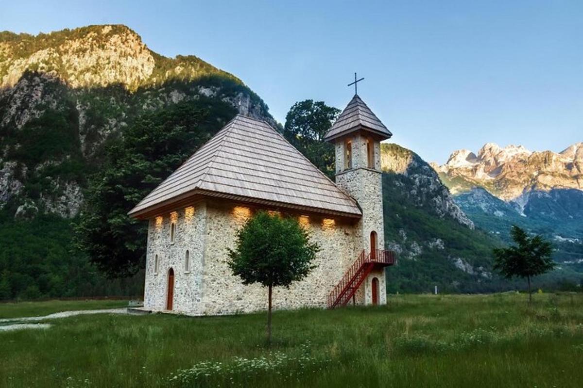 una chiesa in un campo con le montagne sullo sfondo