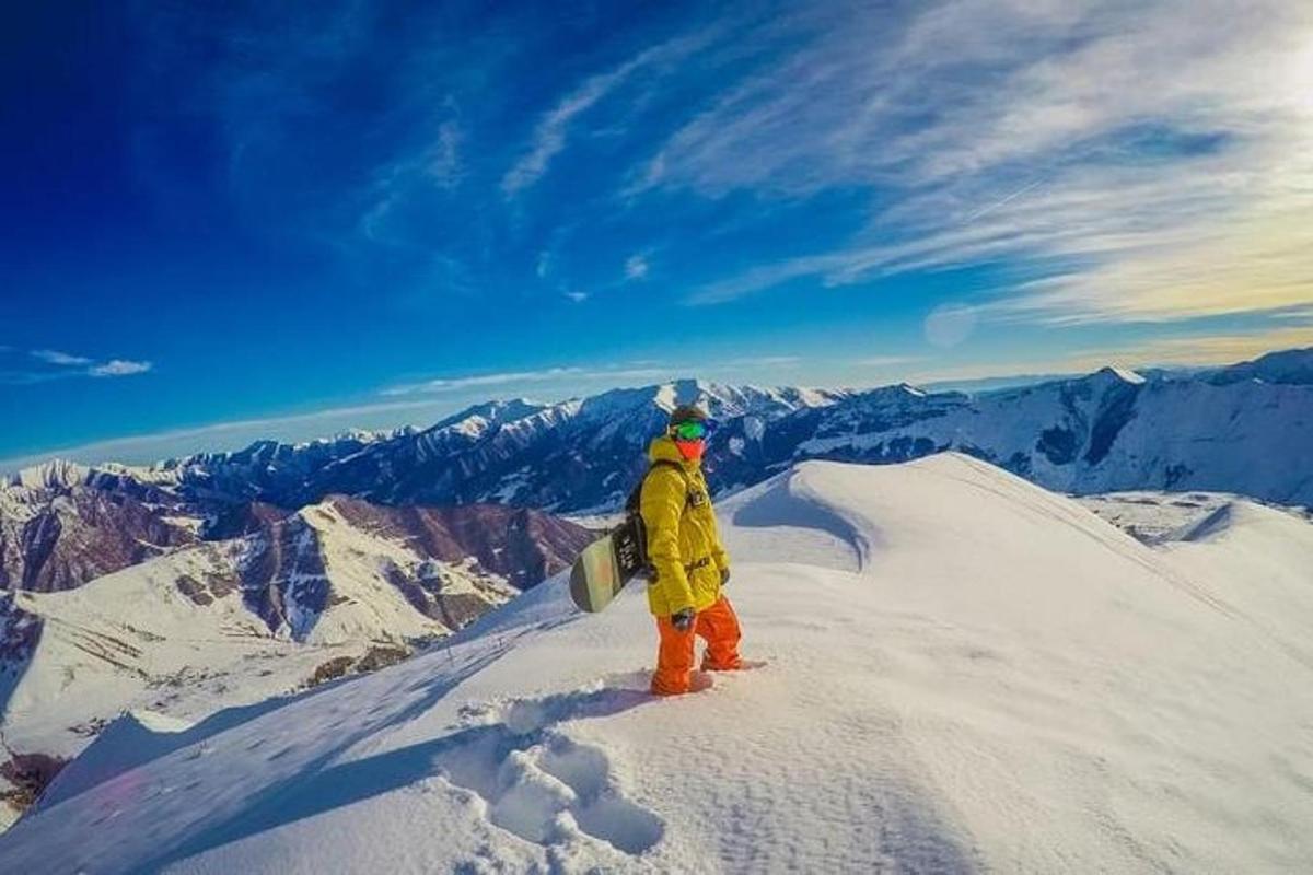 seseorang berdiri di puncak gunung dengan papan seluncur salju