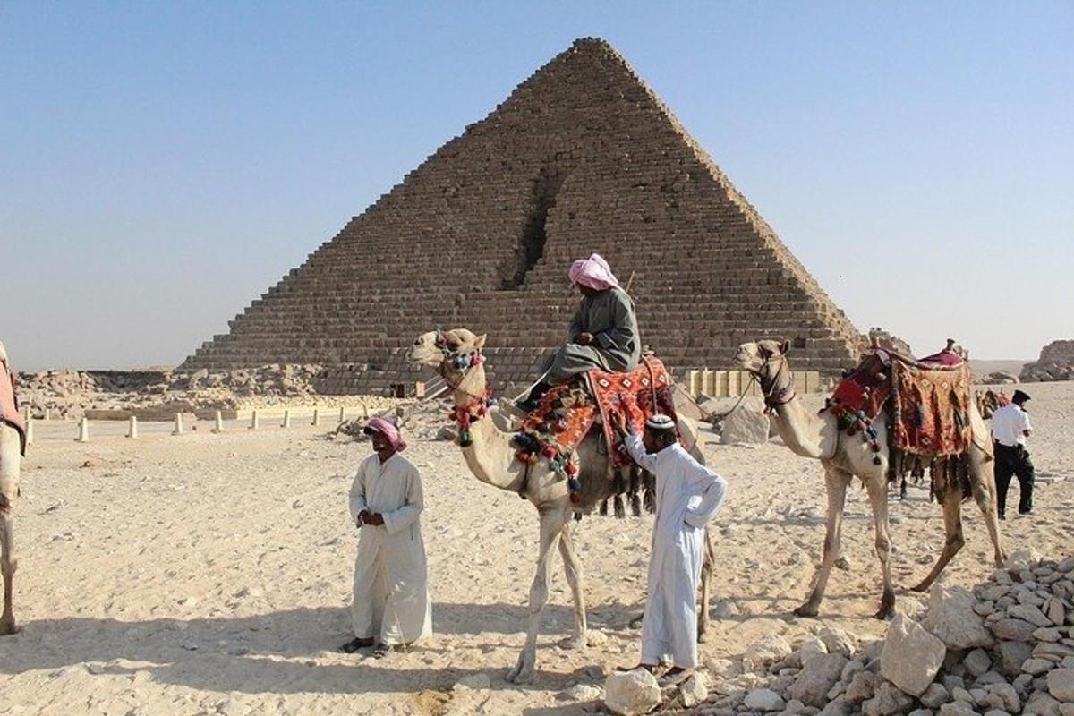 un gruppo di persone a cavallo di cammelli davanti a una piramide