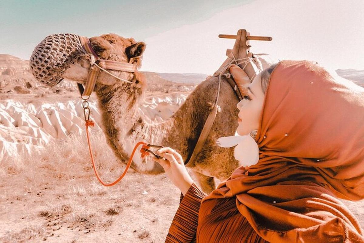 a woman sitting next to a camel in the desert