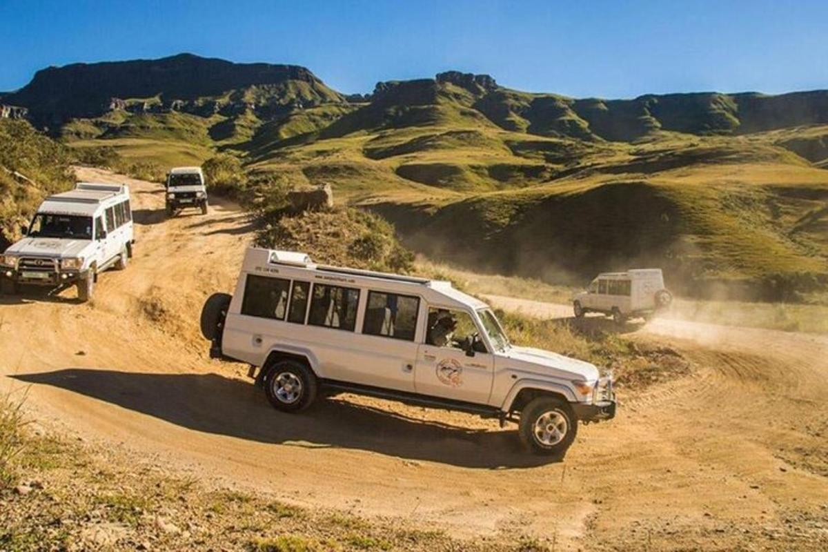 một chiếc xe jeep màu trắng và hai chiếc xe tải trên một con đường đất