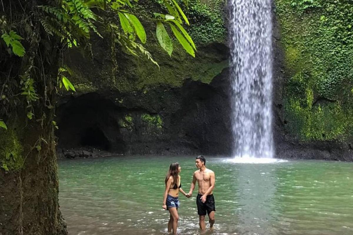 um homem e uma mulher parados na água em frente a uma cachoeira