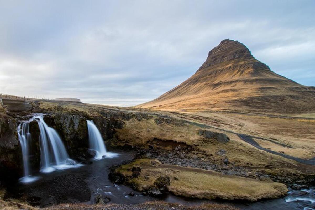 a waterfall in a field with a mountain in the background