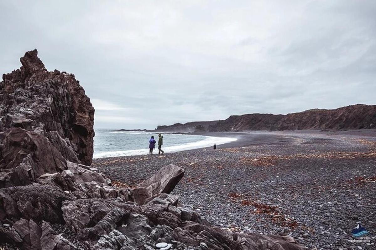 two people walking on a rocky beach near the ocean