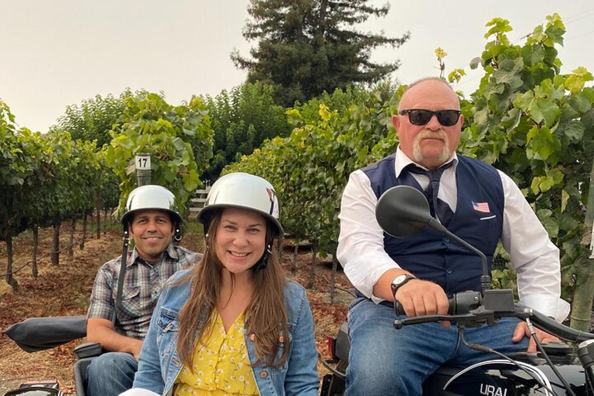 a group of three people riding on a motorcycle in a vineyard