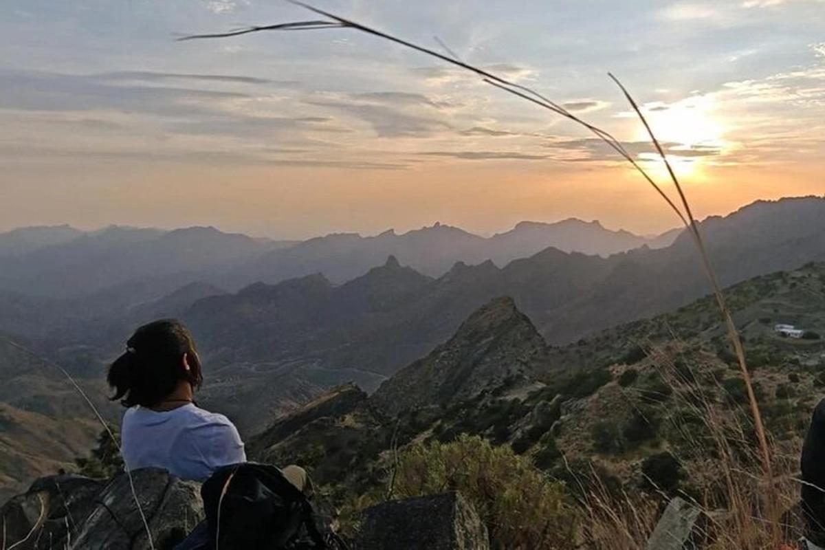 a woman sitting on top of a mountain watching the sunset