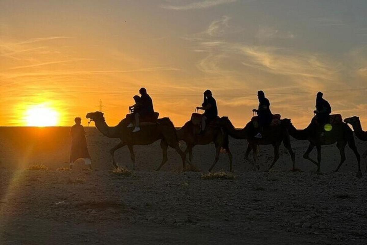 a group of people riding camels in the desert at sunset