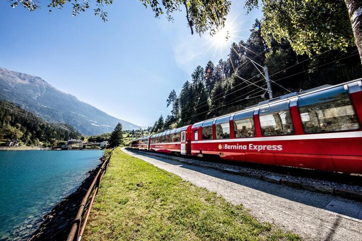 a red train traveling down the tracks next to a lake