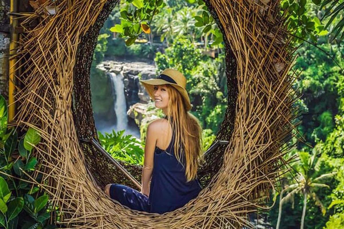seorang wanita sedang duduk di bingkai akar pokok dengan air terjun