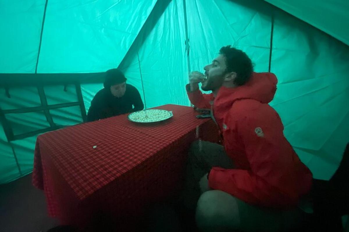 a man sitting at a table in a tent eating