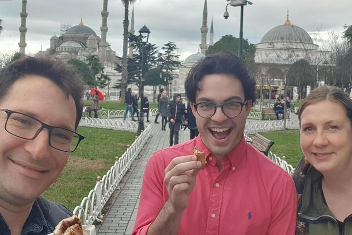 two men eating food in front of a mosque