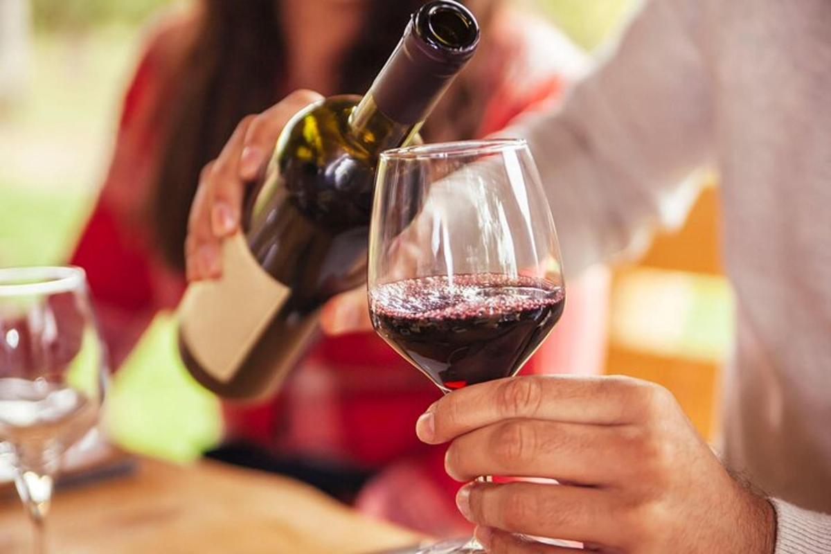 uma pessoa servindo uma taça de vinho tinto