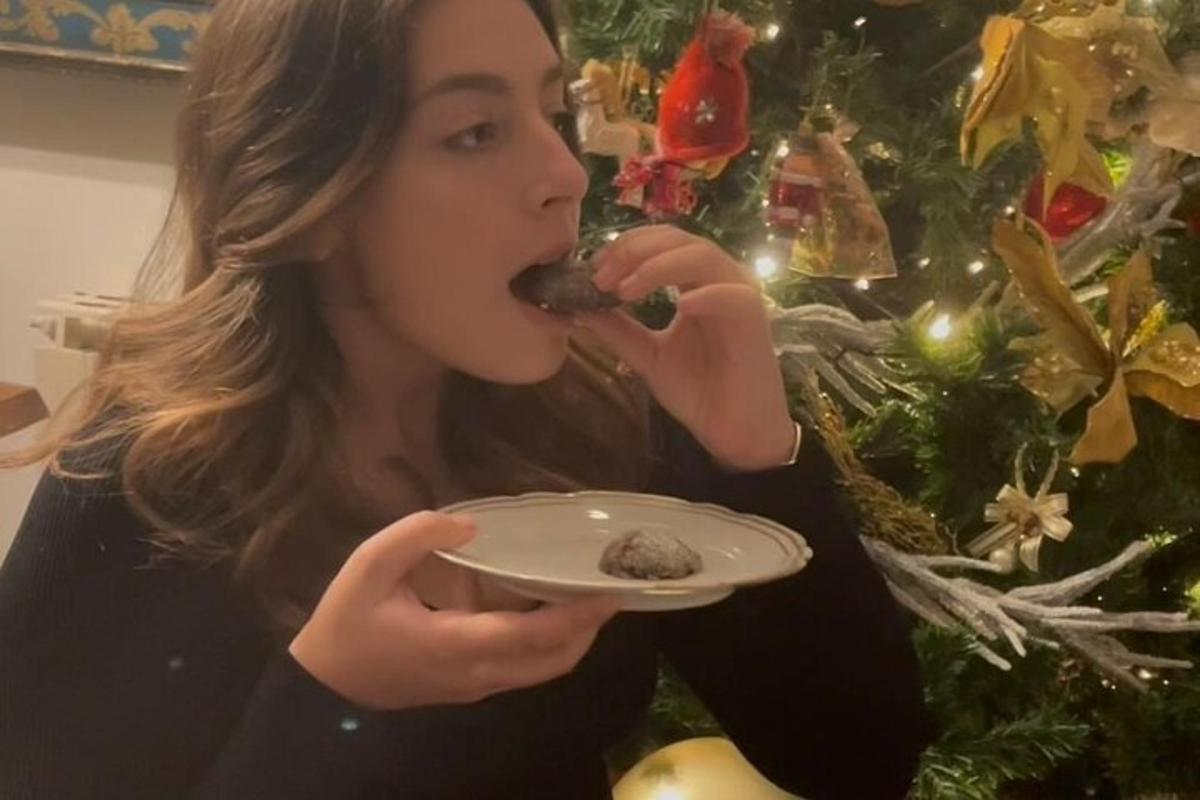 Una mujer comiendo un trozo de comida en un plato cerca de un árbol de Navidad.
