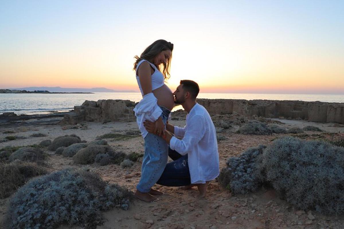 a man holding a pregnant woman on the beach