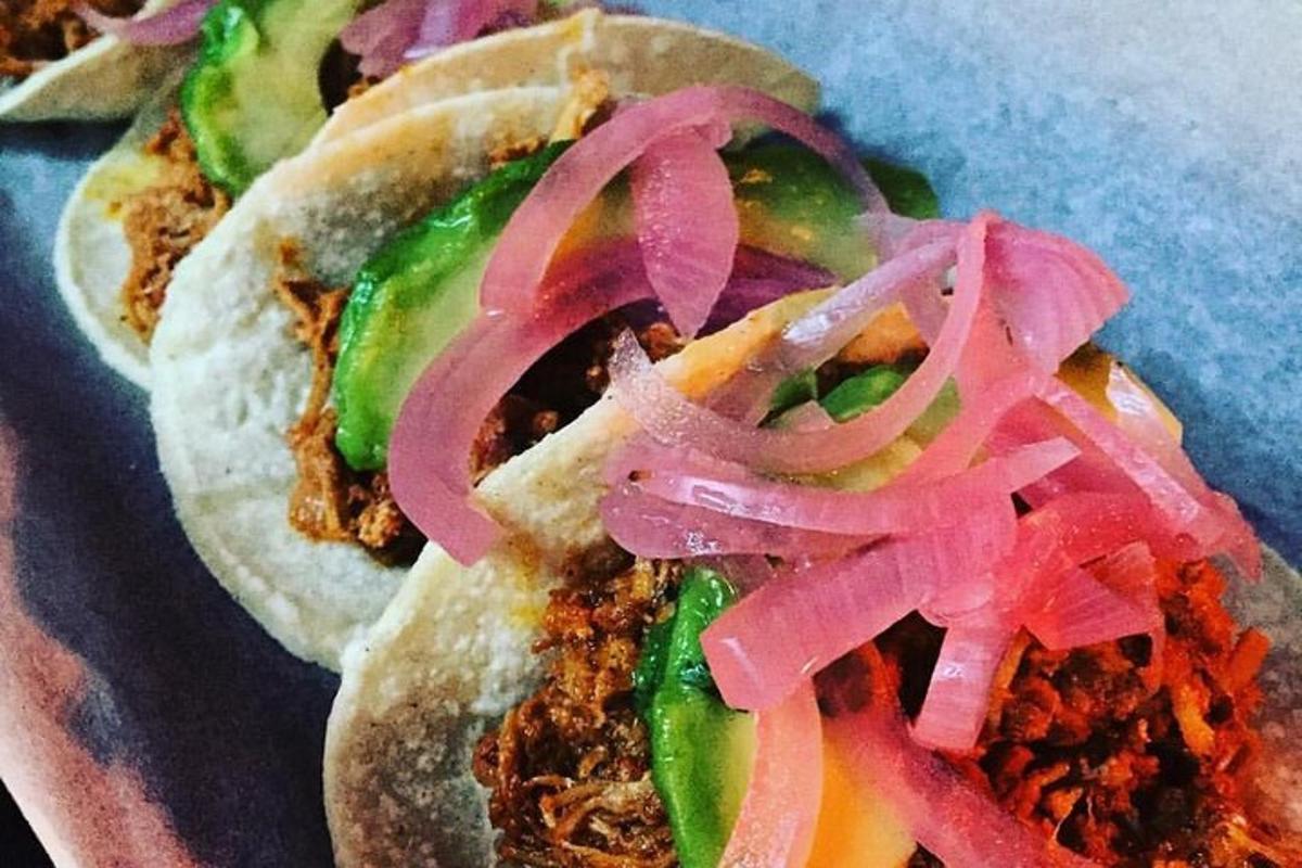 Dos sándwiches de cerdo desmenuzado con cebollas y pepinillos en un plato