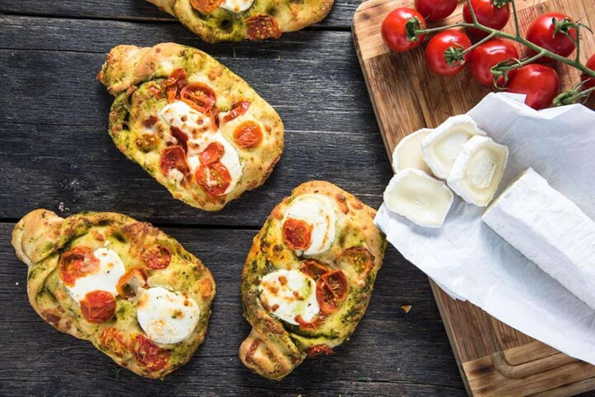 fire små pizzaer på et treskjærebrett med tomater