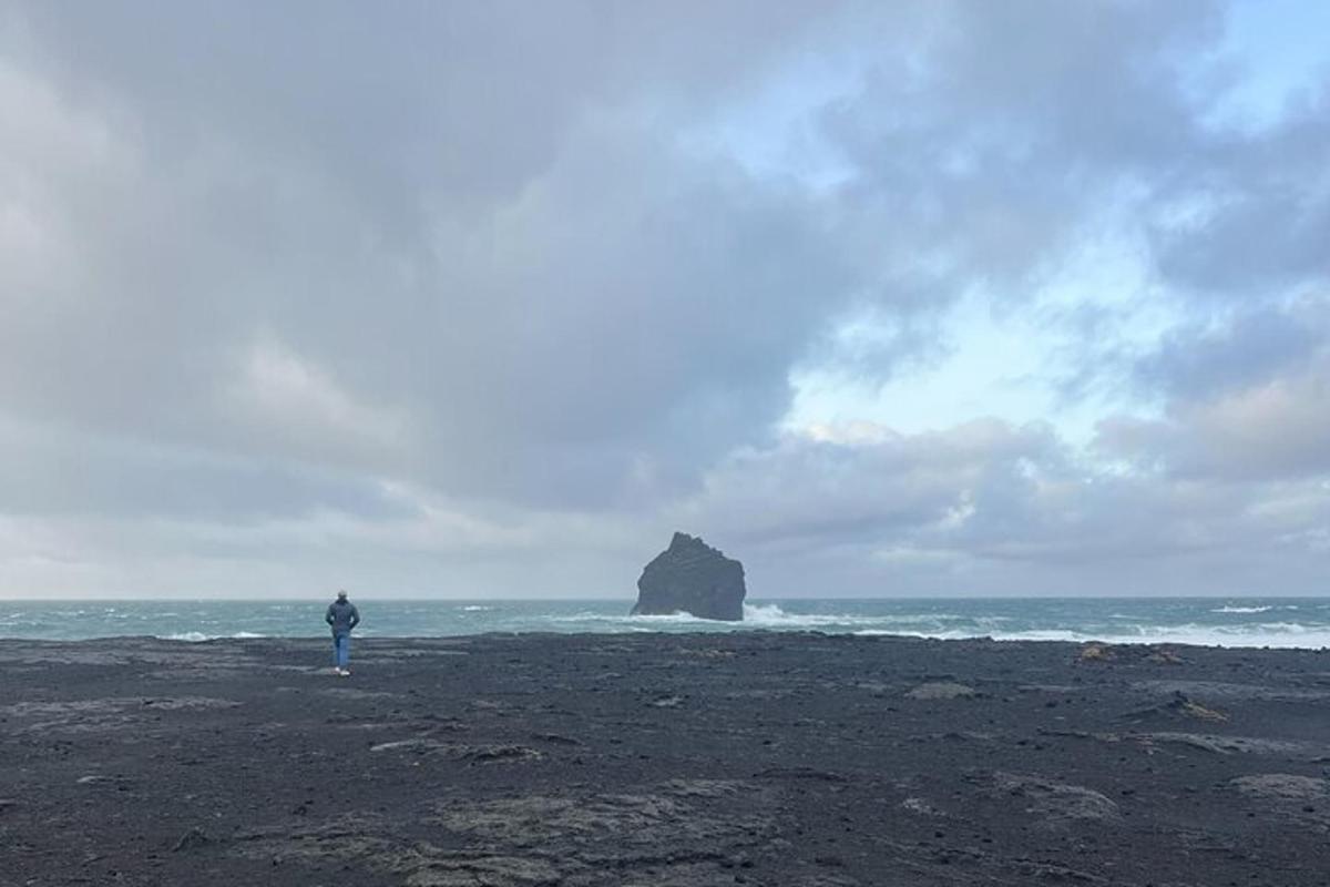 maður stendur á strönd með stein í sjónum