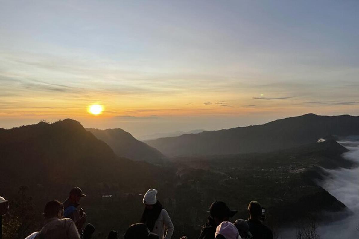 Un grupo de personas de pie en una montaña mirando la puesta de sol.
