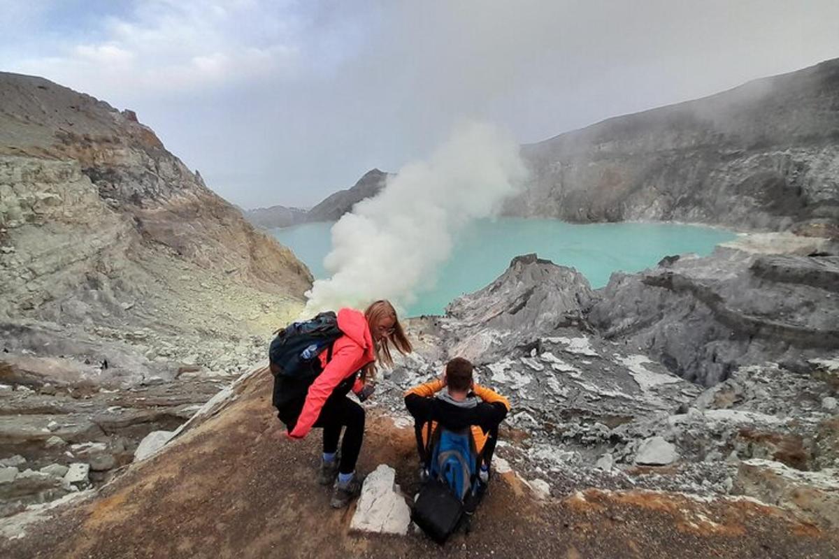 two people on a mountain looking at a geyser