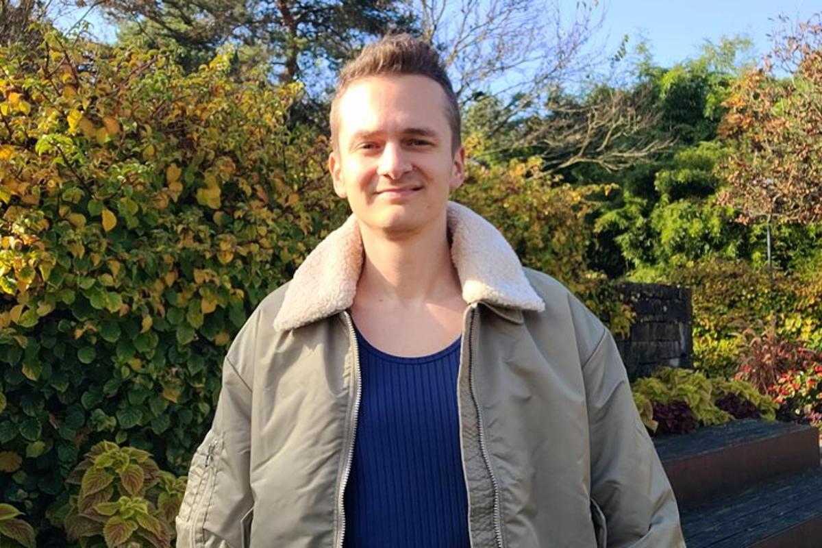 a man in a jacket standing in front of a hedge