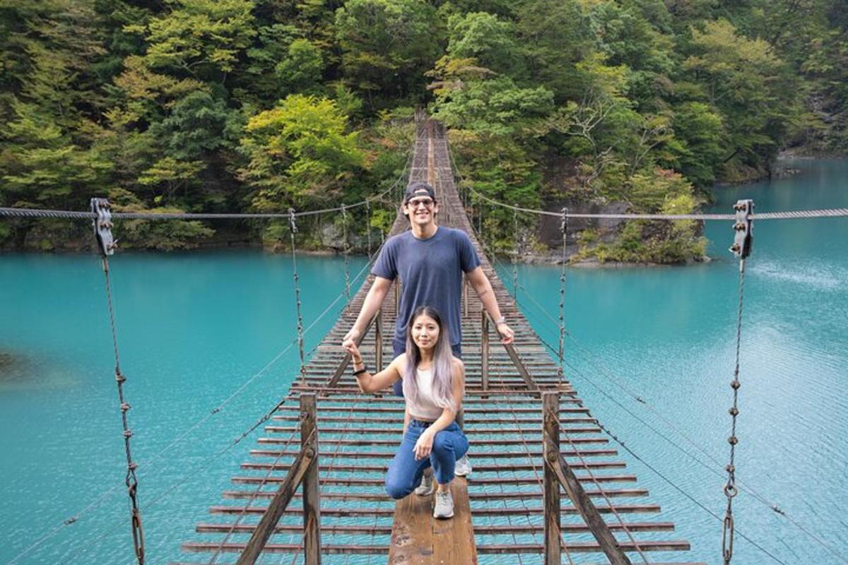 a man and woman posing on a suspension bridge over a river