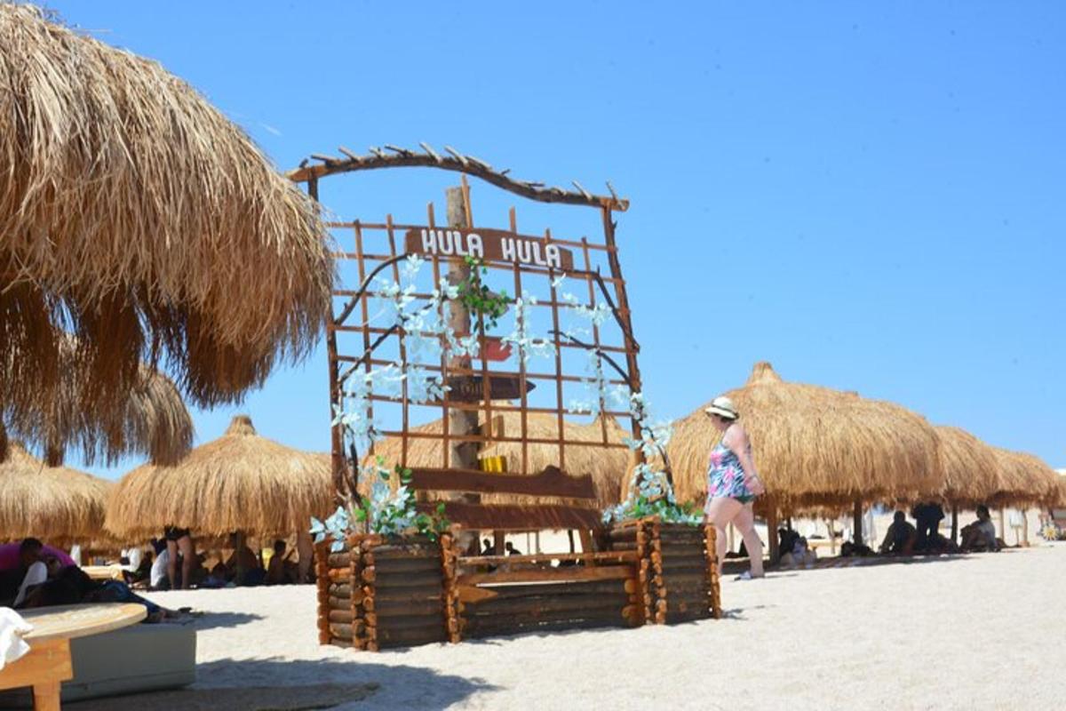 Un cartel en una playa con algunas sombrillas de paja.