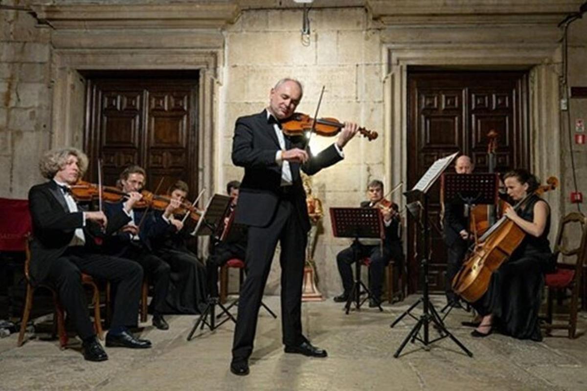 muž hrající na housle před orchestrem