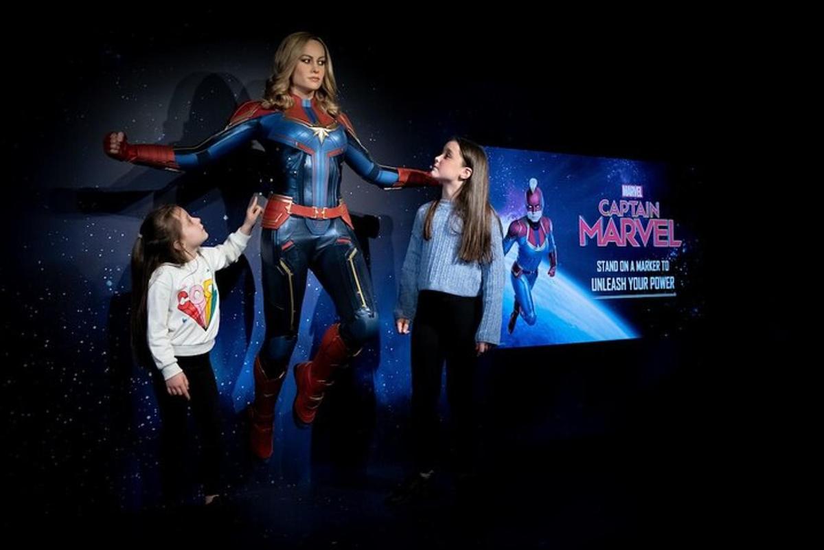 a group of children standing next to a statue of a superhero
