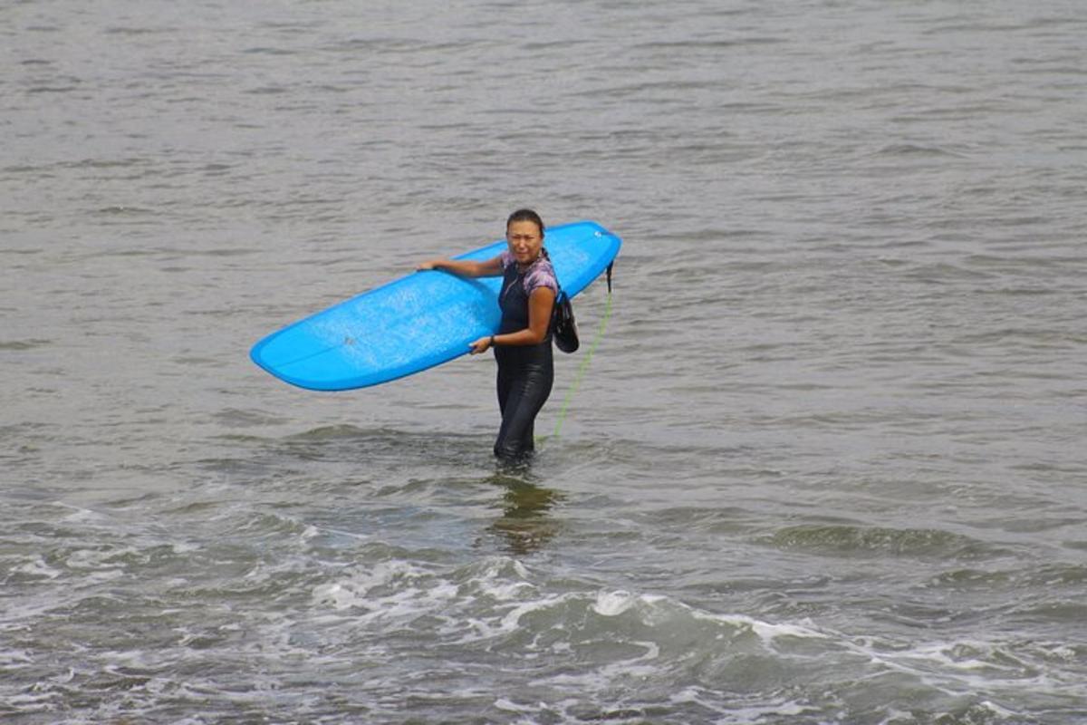 una donna in piedi nell'acqua che tiene in mano una tavola da surf blu