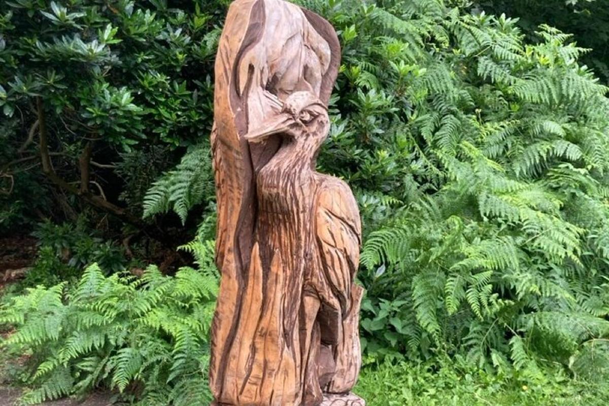 a wooden statue of a person standing next to plants