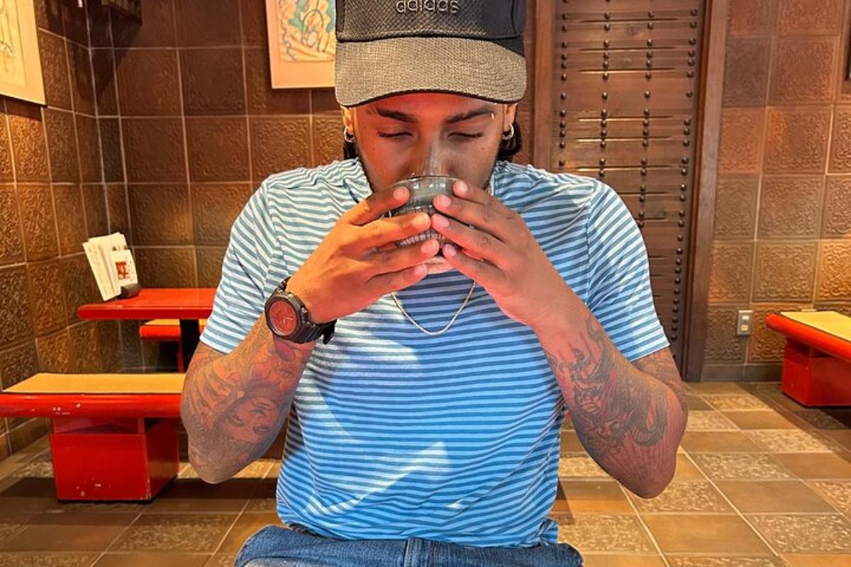 a man with tattoos on his arms drinking from a cup