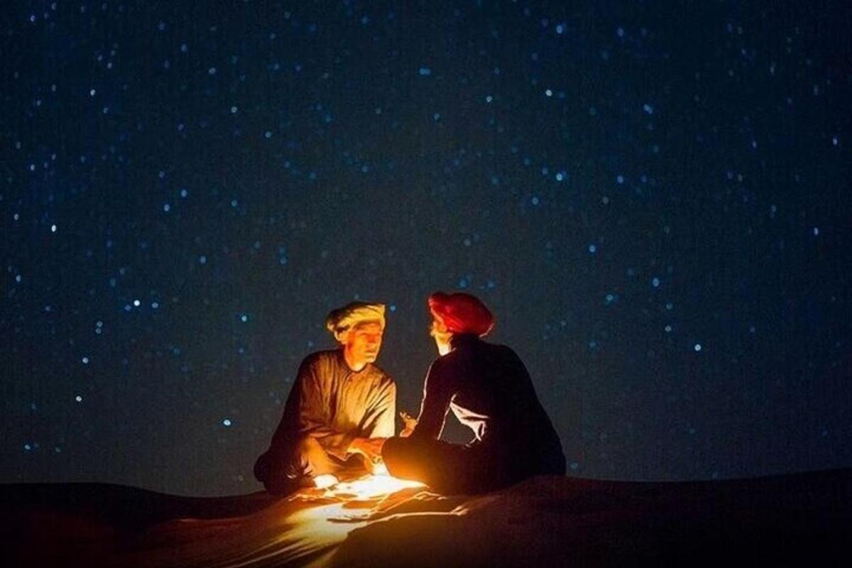 a couple sitting in front of a fire in the desert