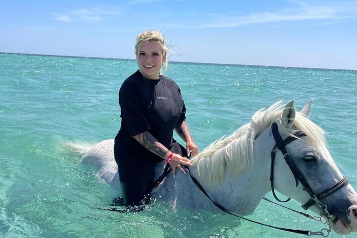 en kvinde, der står ved siden af en hvid hest i havet