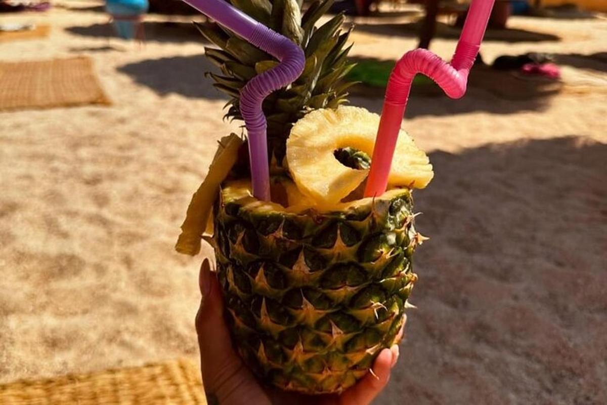 Mâna unei persoane care ține o băutură cu ananas și două cocktailuri