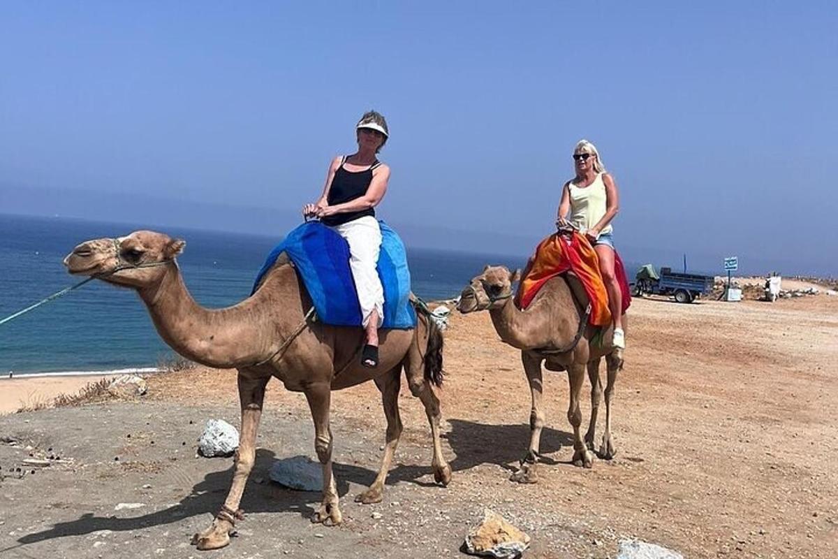 two women riding on camels on a beach