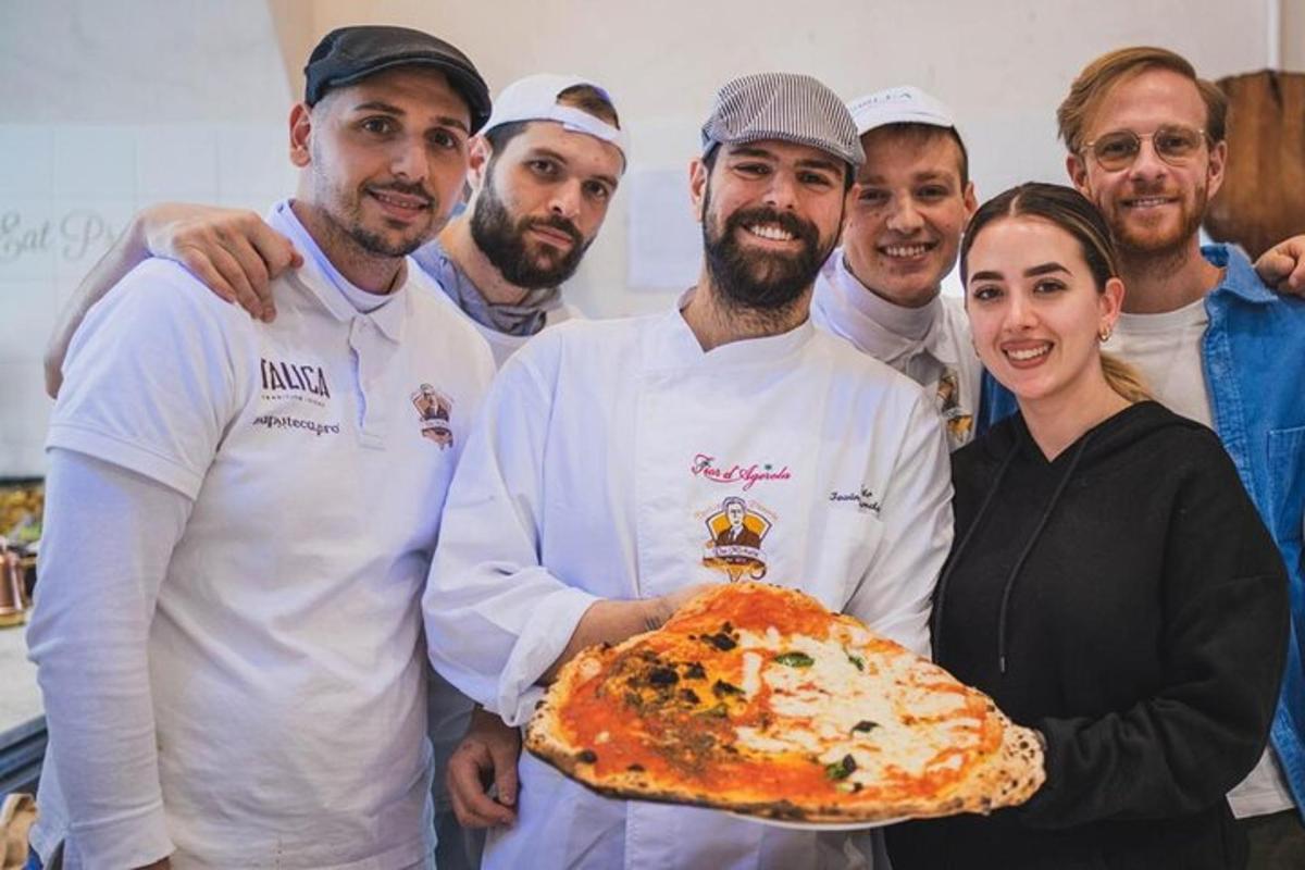 Una mujer sosteniendo una pizza con un grupo de chefs.