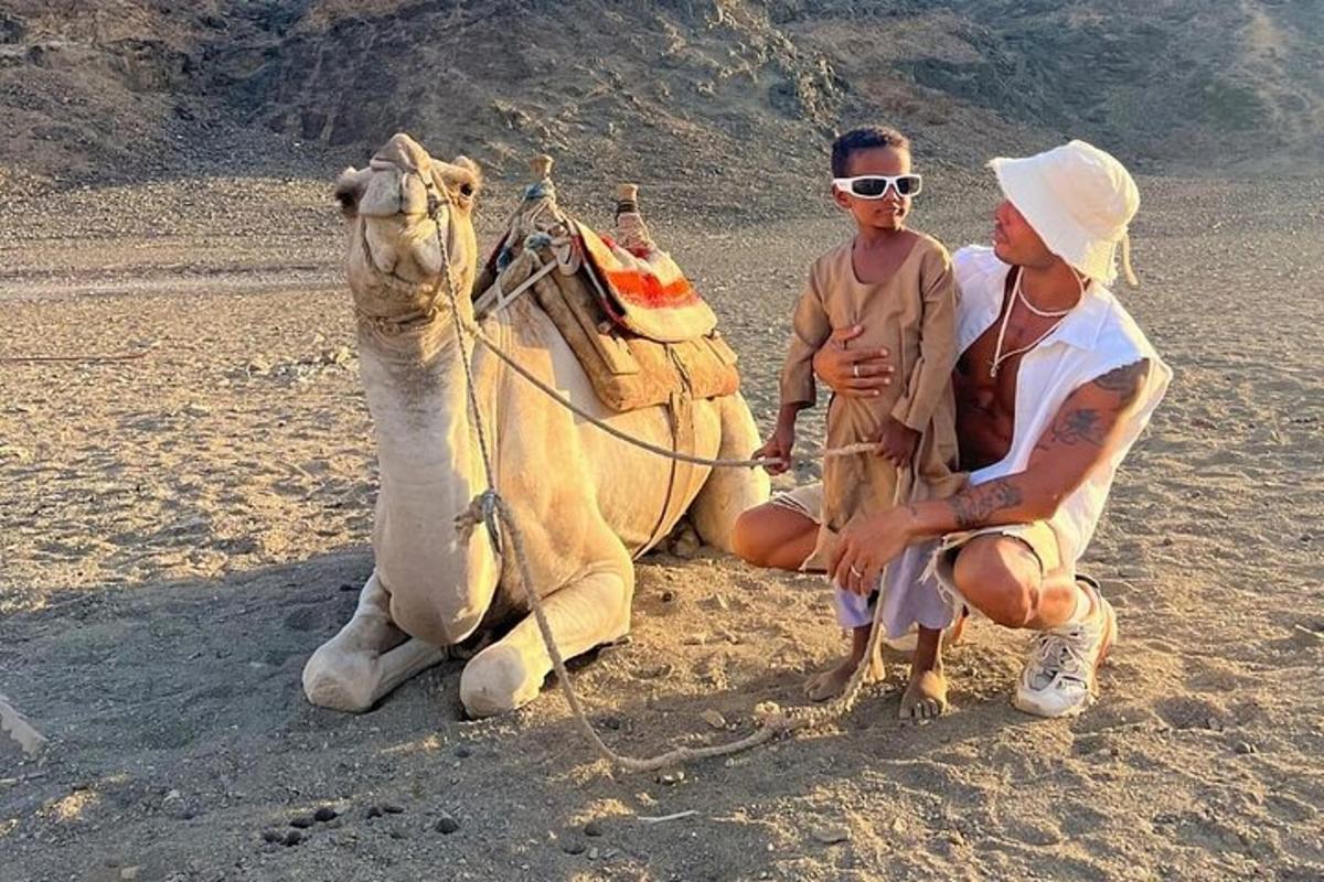 un uomo seduto accanto a un cammello sulla spiaggia