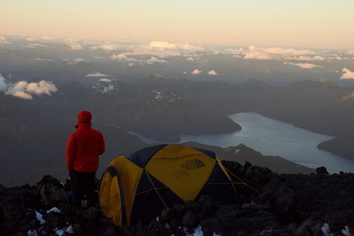 a man standing on top of a mountain next to a tent