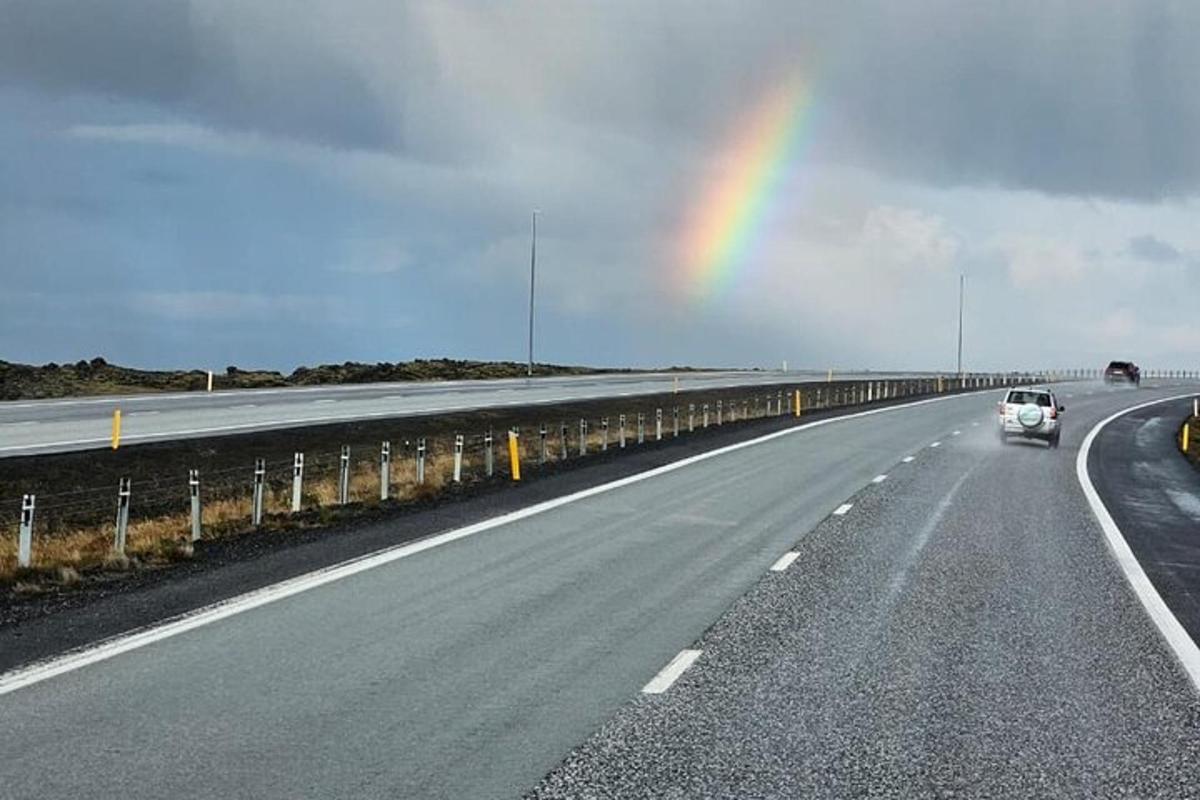 un arcobaleno nel cielo sopra un'autostrada con un'auto