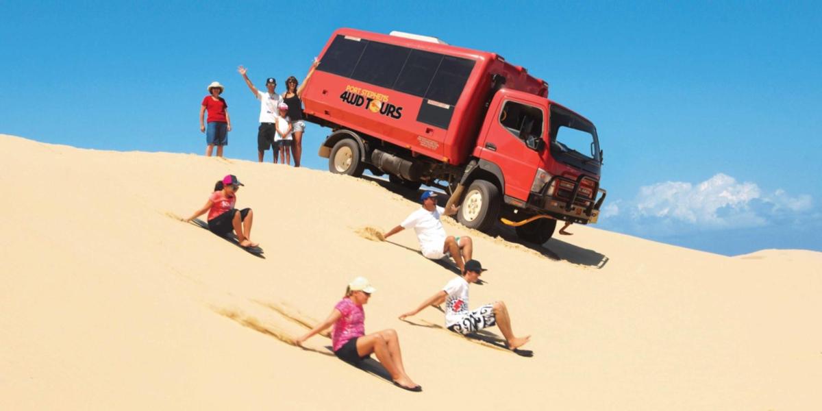 eine Gruppe von Menschen, die im Sand vor einem roten Lastwagen sitzen