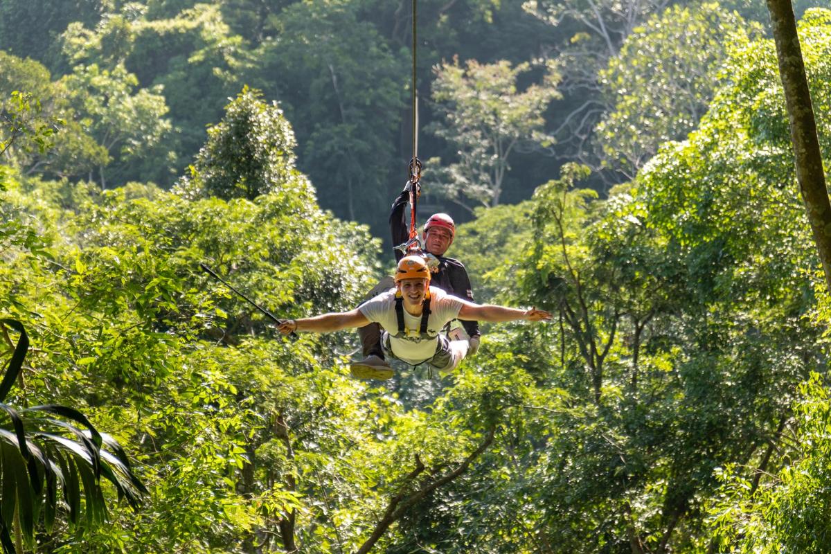 dua orang zip lining melalui pokok di dalam hutan