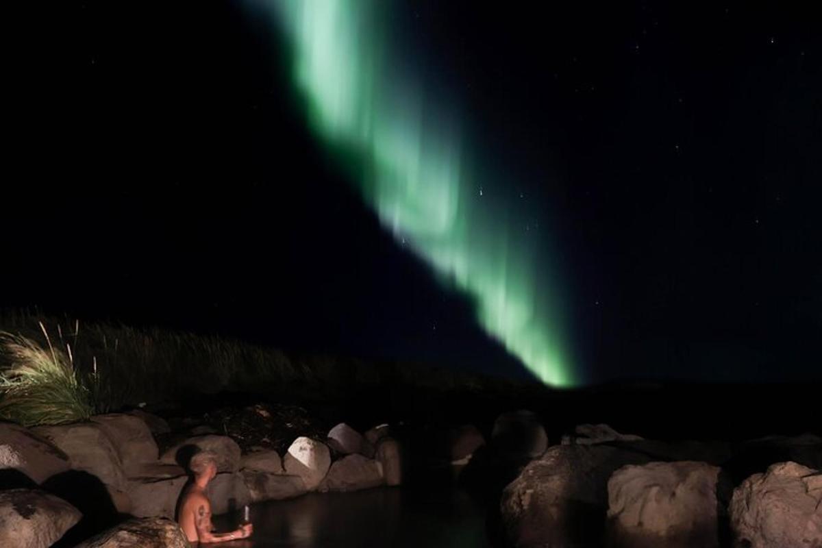 maður situr á klettum undir norðurljósum
