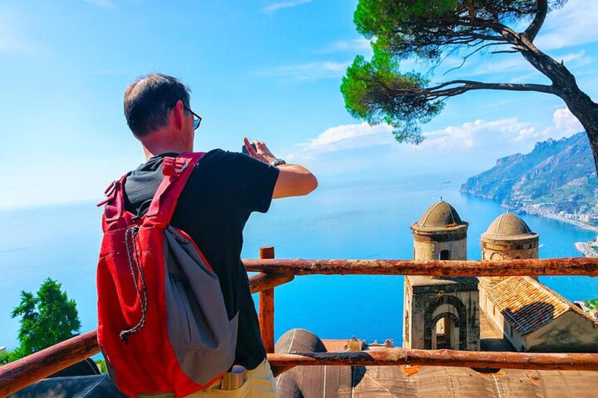 un uomo con uno zaino in piedi su una recinzione che guarda l'oceano