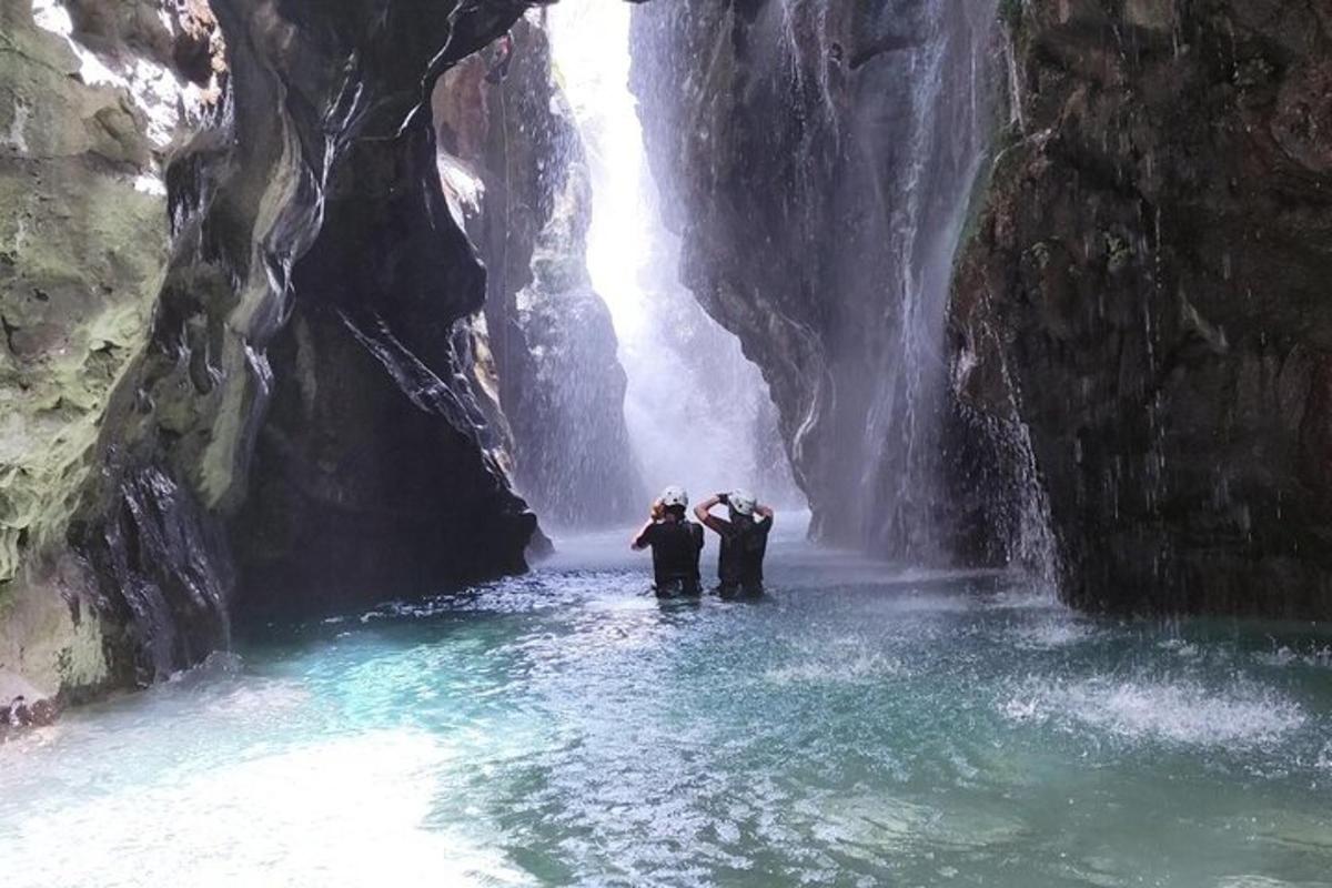 dua orang berdiri di dalam air berhampiran air terjun