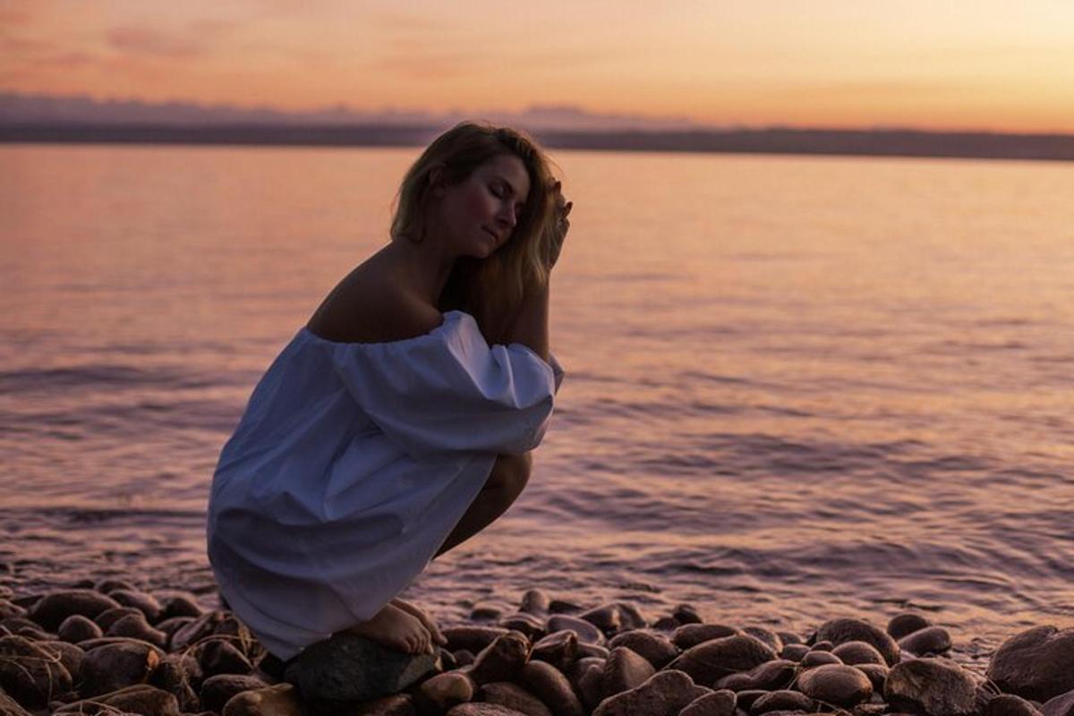 Una mujer con un vestido blanco sentada en una playa rocosa
