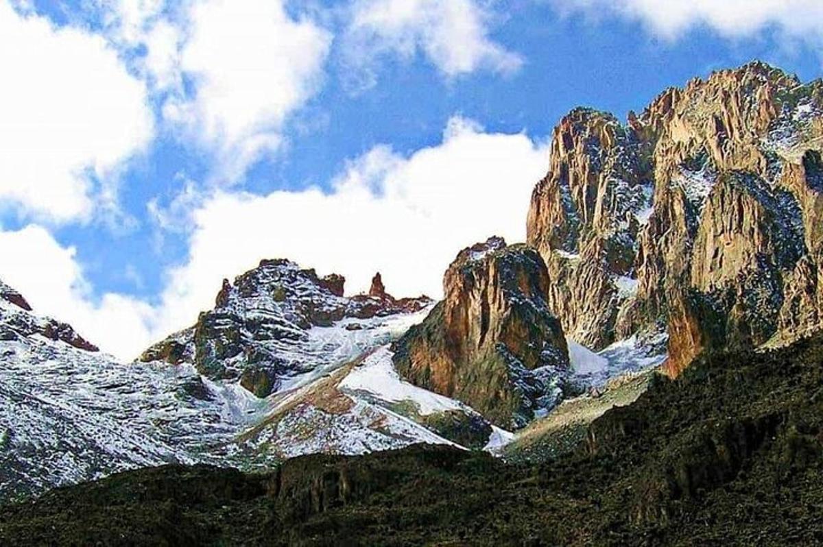 gunung berbatu dengan salji di atasnya dan awan di langit