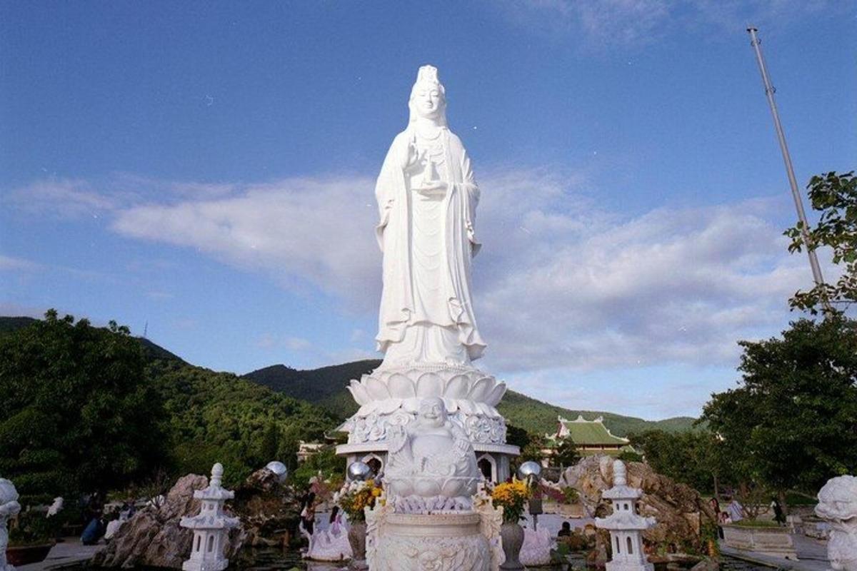 a large white statue in a park with mountains in the background