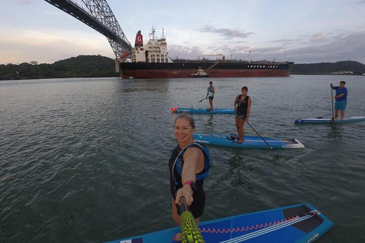 een groep mensen op paddleboards in het water met een schip