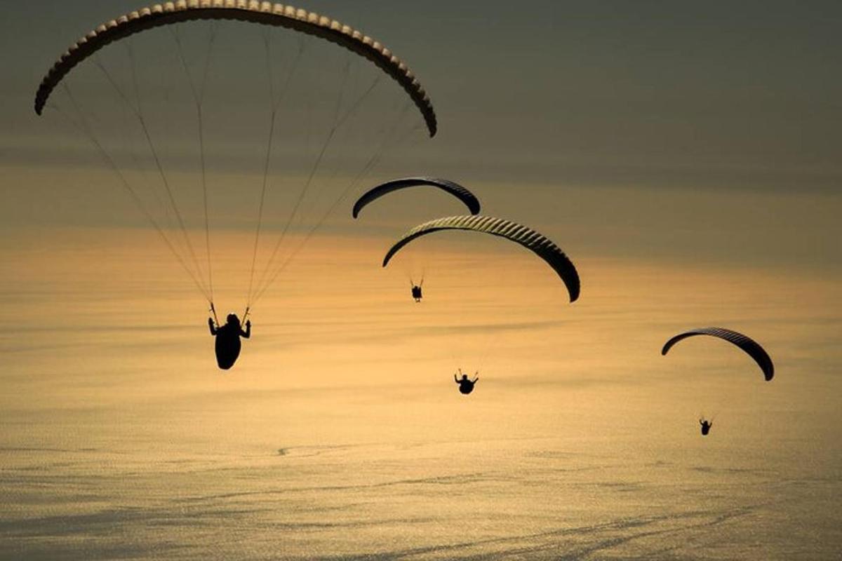 três pessoas estão saltando de paraquedas no céu sobre o oceano